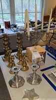 Wide view of all candle holders including brass, pewter holders, and candles on table.