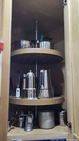 Photo showing metal kettle, coffee pots, mixing bowl, and other metal kitchen accessories inside a cabinet.