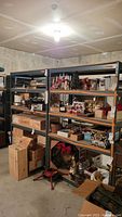 Wide-angle photo showing two metal shelving units filled with miscellaneous household items. Shelves appear to be particle board and frames are metal with a blue-grey paint. Shelves are measuring 48x24 inches and height 72 inches.