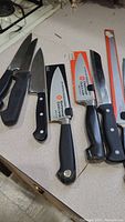 Kitchen knives laid out on counter showing different brands and types including OXO cleaver and Henckels bread knife
