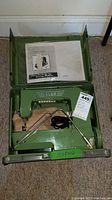 Overall view of green Elna sewing machine in open carrying case with user's manual on lid