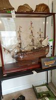 Front view: wooden model ship in dark wood frame with clear acrylic panels and framed cross-section art below