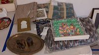 Wide view of assortment of batik fabrics, folded bedspread, brass platter with counterweights, and brass-framed mirror