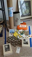 Photo showing a curling metal trivet, Keith Haring yellow dancing figure print, a cylindrical Woodstock Inn waste can, tubular shipping container, and framed black and white photo