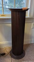 Full view of tall wooden pedestal with fluted column sides and circular base, showing overall shape and design.