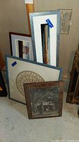 Collection of four framed art pieces leaning against wall, including vintage photo, mandala print, and other prints