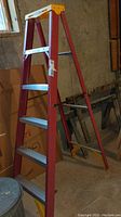 Side view of the red Werner fiberglass step ladder showing four aluminum steps and yellow top cap.