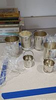 Six sterling silver cups displayed on countertop wrapped in protective plastic