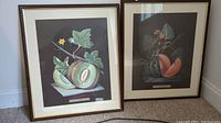 Two framed prints leaning against wall showing both melon and watermelon illustrations
