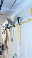 Yard tools hanging on garage wall including rakes, shovels, clipper shears, and others representing various types of yard grooming tools.