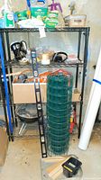 Shelf displaying various yard chemicals, tools, chicken wire roll, metal level, extension cord, and mini grill in basement.