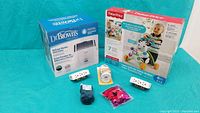 Photo showing boxed Dr. Brown's Deluxe Bottle Sterilizer, boxed Fisher-Price Laugh & Learn Walk 'n Ride Zebra walker, safety door handle covers, multi-plug covers, mittens and toy on blue background.