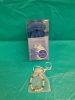 Photo of The Blue Day Book packaged with a blue stuffed frog and a beaded bracelet in a small white organza pouch on a green background.