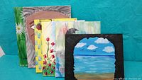 Five large used painting canvases displayed side by side with various painted scenes including ocean, flowers, abstract patterns, portrait, and floral designs.
