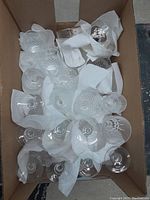 Top-down view of multiple glassware pieces wrapped in paper towels inside a cardboard box, showing different sizes and patterns.