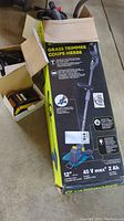 Box with Yardworks 12-inch cordless grass trimmer and battery charger with battery pack beside it.