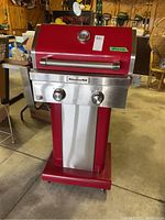 Front view of red KitchenAid propane barbecue grill on pedestal base with two stainless steel control knobs