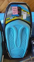 Top view of the kneeboard showing blue foam padding with wing-like design and colorful graphic decals.