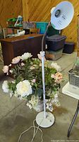 Full view of the white metal floor lamp positioned next to the large faux flower arrangement in a white pedestal planter.