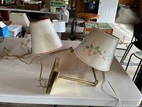 Two extendable wall lamps with floral patterned shades on a table, with brassy metal arms and elbows for extension and rotation.