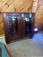 Front view of wooden cabinet with two decorative leaded glass doors and brass handles.