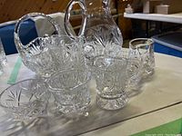 Cut glass pitcher, basket, butter dish, sugar bowl, pourer, and glasses on table