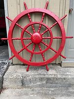 Front-facing view of red ship's wheel leaning against exterior wall