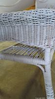 Close-up photo of a white wicker table showing woven wicker detail on the tabletop and lower shelf, along with one leg wrapped in wicker material.