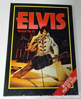 Front cover of the Elvis musical pop up book showing Elvis Presley in white stage outfit playing guitar.