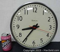 Front view of SIMPLEX industrial clock with 13-inch diameter showing clock face, numerals, hands, and red second hand along with a soda can for size reference.