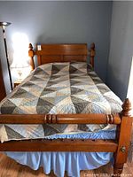 Full view of the full size wooden bed with headboard and footboard, with bedding and a quilt covering the mattress area.