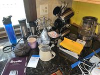 Photo of the kitchen counter showing Breville tea maker, tea pots, coffee mugs, Keurig water filter cartridges, travel mugs, and coffee pod holder rack with accessories.