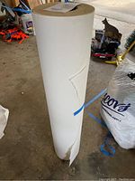 Full view of a large roll of white craft paper with some minor tears at the bottom edge, standing upright on the ground in a garage or workshop environment.
