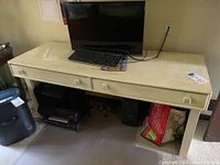 Photo of cream painted work desk with two drawers showing keyboard and monitor placed on top, desk surface visible with some dirt marks and wear.