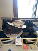 Collection of various hats including cowboy hats in a laundry room basket