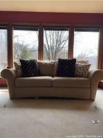 Front view of the beige and gold toned upholstered sleeper sofa with scroll arms, four included throw pillows visible.