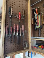 Photo showing multiple screwdrivers with red and black handles arranged on pegboard with other hand tools