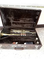 Brass trumpet in open brown hard case with velvet lining, showing intact tubes and valve buttons.