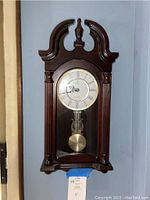 Full view of Verona wooden wall clock with glass door showing pendulum and decorative top.