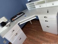 White L-shaped corner desk with drawers and hutch, accompanied by white rolling desk chair