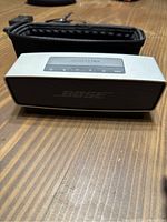 Front angle showing the Bose SoundLink Mini Bluetooth speaker with the front speaker grill and control buttons on top with case in background.