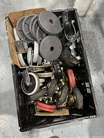 Top view of black plastic crate filled with assorted caster wheels and mounting plates, showing various sizes and materials.