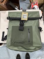 Front view of the green Filson dry backpack with roll-top buckle and front zip pocket.