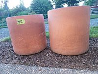 Two large terra cotta pots placed side by side on mulch, showing their cylindrical shape and terra cotta color.