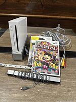 Nintendo Wii console standing vertically with power and AV cords, sensor bar, and Carnival Games in front with measuring tape included for size reference.