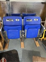 Pair of blue stadium seats with Seattle Seahawks logo and attached metal side frames labeled 11 and 12.