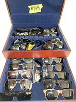 Photo of wooden box with blue velvet interior showing various sunglasses in two-layer compartments.