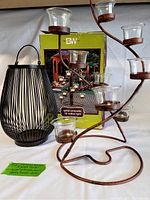 Umbrella spiral metal votive candle holder with 10 clear glass holders and original box, next to black metal cage lantern with handle.