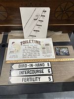 Overall lot on wood surface showing all items including Toilettine sign, Wall Street diagram, music album, and four vintage signs with ruler for scale.