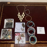 Photo of all jewelry items arranged on a burgundy surface including box of mixed items, bracelets, and necklaces